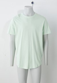 Šviesiai žalios spalvos, tekstūruota medvilninė marškinėlių suapvalinta apykakle, trumpomis rankovėmis ir išlenktu kraštu. Matomų raštų ar metalinių detalių nėra.