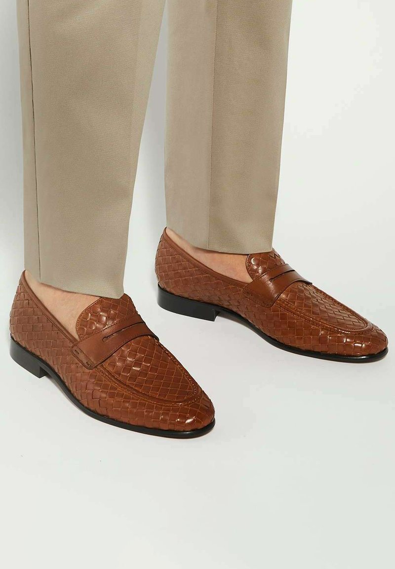 Brown woven leather loafers with a smooth finish, featuring a decorative band across the vamp and a low-profile black sole.