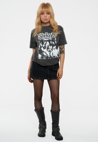 Black graphic t-shirt featuring white band logo and imagery, paired with a black denim skirt and knee-high black boots with decorative buckles.