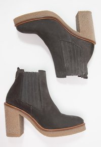 Harmaat mokkanahka nilkkakengät, joissa on joustavat sivupaneelit, teksturoitu beige paksujalkainen korko ja ruskea reunus pohjan ympäri.