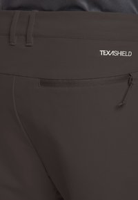 Dunkelbraune Hose mit glatter Textur, ausgestattet mit einer Reißverschlusstasche und einem verstellbaren Bund. Das "TEXASHIELD"-Logo ist prominent angebracht.