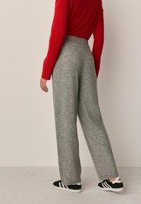 Grå strikkede bukser med vid ben og høj talje, der har ribbet struktur og to sidesømme. Sammen med en klar rød sweater og sorte sneakers.