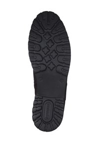 Semelle en caoutchouc noir avec un relief texturé, présentant plusieurs motifs d'adhérence et une section de marque au centre.