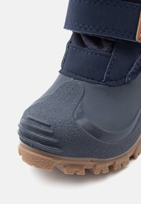 Niebieskie, wodoodporne buty z teksturowanym gumowym wykończeniem, wzmocnionym noskiem, regulowanym paskiem i brązową, karbowaną podeszwą dla lepszej przyczepności.