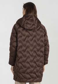 Brązowa kurtka puchowa z kapturem, o pikowanej fakturze i falistym wzorze. Długie rękawy i luźny krój, sięgająca do połowy uda.