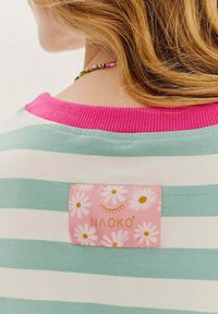 Pruhované tričko s mätovo-zelenými a bielymi pruhmi, ružovým rebrovaným golierom a ružovou etiketou s bielymi sedmokráskami a zlatým písmom.