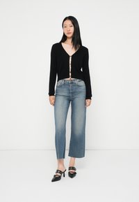 Cardigã preto cropped com decote em V e detalhes em botões dourados, combinado com jeans flare azul claro e mules pretas de salto.