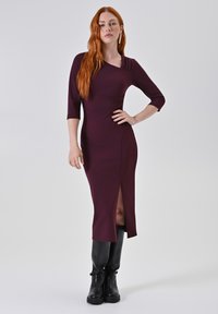 Bordeaux dress met aansluitende pasvorm en driekwart mouwen, met zij-split detail en gestructureerde schouderaccenten. Gekocht met hoge zwarte laarzen tot de knie.