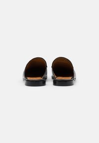 Sorte skinn slip-on sko sett fra baksiden, med en glatt tekstur, rund tå og et enkelt, minimalistisk design med flat såle.