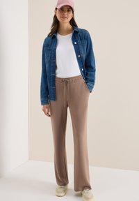 Denim overhemd in blauw, witte t-shirt, beige broek met elastische taille, lichtkleurige sneakers en roze pet; casual, relaxte pasvorm, zichtbare knopen.