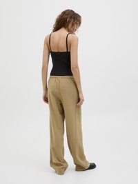 Svart ribbet tanktopp og løse beige bukser. Buksene har elastisk midje. Modellen er sett fra baksiden mot en hvit bakgrunn.