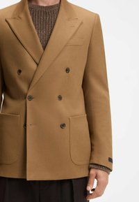 Blazer in misto lana marrone a doppio petto con revers, due tasche frontali e bottoni neri. Maniche lunghe con dettagli in maglia sui polsini.