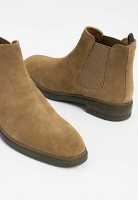 Botas de tobillo de ante marrón con paneles laterales elásticos, puntera redondeada y un bajo tacón apilado, que cuentan con una parte trasera texturizada para un detalle adicional.