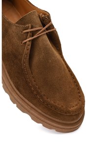 Brown suede shoe featuring a rounded toe, minimal lacing, and a thick, textured rubber sole with subtle contours.