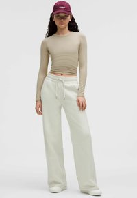 Maglietta beige a maniche lunghe, pantaloni bianchi a vita alta e berretto bordeaux. Tessuto morbido, vestibilità comoda, vita regolabile con cordino, pantaloni alla caviglia.