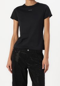 Sort bomulds t-shirt med korte ærmer og rund halsudskæring. Har et lille hvidt "Calvin Klein" logo på brystet. Glat tekstur.