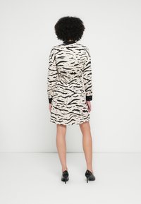 Šaty s motívom zvieracej potlače so svetlohnedým podkladom a čiernymi tigrovanými pruhmi, dlhými rukávmi, elastickým pásom a rovnou lemovkou. Čierne podpätky.