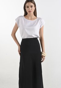 Top bianco a maniche corte abbinato a una gonna maxi nera. Il top presenta un collo rotondo; la gonna ha una texture e una vestibilità lisce e aderenti.