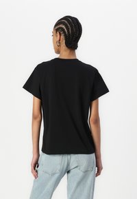 Black short-sleeve t-shirt with a crew neck, made of soft fabric. The back features a clean, simple design, tucked into light blue jeans.