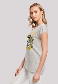 Grå bomull T-skjorte med rund hals, korte ermer og et Hufflepuff-våpenskjold i gul, svart og hvit på forsiden.
