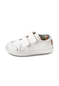 Zapatillas infantiles blancas con dos correas de velcro, punta de goma y forro interior de cuadros de colores sobre un fondo blanco.
