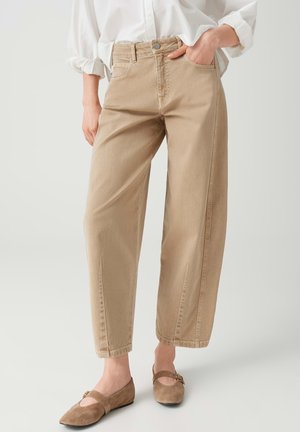 Persona che indossa pantaloni beige a gamba dritta, camicia bianca con le maniche arrotolate e ballerine Mary Jane in camoscio marrone con fibbia.