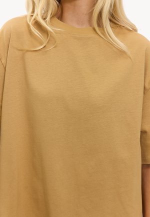 T-shirt beige à manches courtes, coupe ample, en coton doux, avec un col rond et une texture lisse, dotée de détails de couture minimalistes.