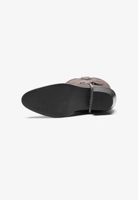 Brauner Lederstiefel mit strukturierter Oberfläche, versehen mit einer Kettenakzentuierung am Knöchel und einer schwarzen Gummisohle mit horizontalen Linien.