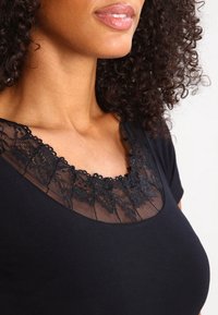 Top negro con escote de encaje y debajo de malla, mangas cortas y un diseño ajustado. Textura suave y patrón de encaje detallado.
