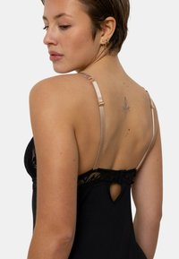 Lingerie en dentelle noire avec un détail en trou de serrure, des bretelles nude ajustables et un tissu texturé. Design ajusté avec des accents en dentelle intriqués.