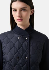 Marynarska pikowana kurtka z teksturowanym wzorem diamentowym, z żebrowanym kołnierzem i metalowymi guzikami napowietrznymi, z gładkimi akcentami na rękawach.