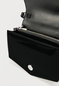 Fekete bőrtáska, amely sima, fényes felülettel, cipzáras rekesszel és patentzáras záródással rendelkezik. Belseje elegáns kialakítású, minimális részletezéssel.