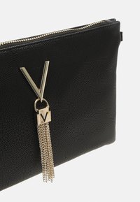 Clutch nera a trama con hardware dorato, caratterizzata da un prominente logo "V" e dettagli con frange a catena, chiusura a zip sulla parte superiore.