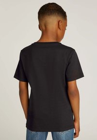 T-shirt nera in cotone con maniche corte, scollo rotondo e orlo dritto, vista da dietro. Abbinata a jeans di denim blu.