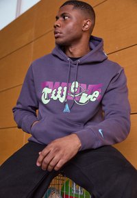 Felpa viola con design di testo audace e multicolore. Materiale in cotone, cappuccio con coulisse e piccolo logo Nike blu sulla manica.