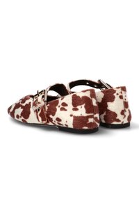 Zapatos planos de punta afilada con un patrón de manchas de vaca en marrón y blanco y correas con doble hebilla plateada.