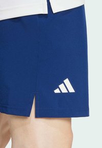 Marina blå sportshorts med en vit Adidas-logotyp. Har ett utskärning på den nedre fållen för ökad rörelsefrihet. Tillverkade av lättviktig tyg.