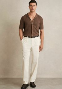 Cămașă maro cu mânecă scurtă, cu un model texturat, cu nasturi, asociată cu pantaloni crema și o curea neagră. Purtați cu pantofi slip-on închiși la culoare.