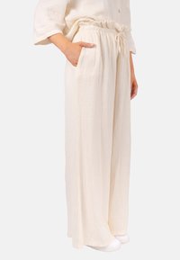 Weite Hosen aus strukturiertem cremefarbenem Stoff, mit einem elastischen Bund und Kordelzug sowie seitlichen Taschen.
