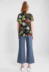 Top corto de flores negras con mangas cortas que presenta flores rojas, verdes y blancas, combinado con pantalones de mezclilla azul de pierna ancha y zapatos de tacón bloque blancos.