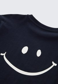 Marineblaues T-Shirt mit einer großen weißen lächelnden Gesichtsgrafik. Aus Baumwollmaterial mit Rundhalsausschnitt und glatter Textur.