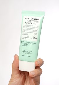 Ljusgrön plastflaska med Benton UV Defense solkräm. Innehåller 50 mL, markerar SPF50+ och veganmärke. Har ett flip-top lock.