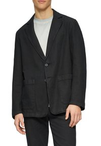 Schwarzer Leinenblazer mit Reverskragen, zwei vorderen Taschen, Ein-Knopf-Verschluss und lässiger Passform. Getragen über einem hellgrauen Hemd.