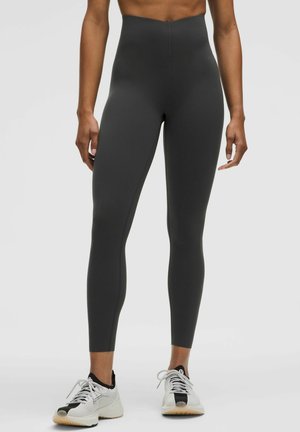 Høj talje, tætsiddende leggings i mørkegrå, lavet af strækbart stof med en glat tekstur. Sæt sammen med hvide træningssko.