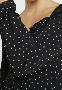 Mustapaita, jossa on kokoontuva kaula-aukko, elastiset hihansuut ja off-white tähti-kuvio koko kankaan läpi. Sileä, kevyt materiaali.
