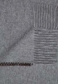 Coperta in misto lana grigia con finitura texture, bordata con frange e un dettaglio cucito di colore marrone scuro in contrasto.