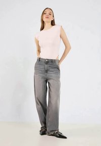 Top justo rosa claro com mangas curtas, combinado com jeans soltos de cintura alta em cinza claro e sapatos baixos pretos de bico fino.