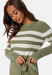 Maglione a righe verdi e bianche realizzato in materiale knit, con maniche lunghe e una cintura annodata in vita. Texture a coste su tutta la superficie.