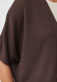 Bruine gebreide trui met een losse pasvorm, korte dolmanmouwen en een V-hals ontwerp. De textuur lijkt zacht en lichtgewicht.