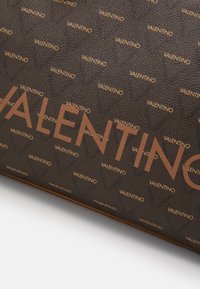 Brown leather bag featuring a repeating "VALENTINO" logo in a lighter shade, with a textured surface and accented borders.
